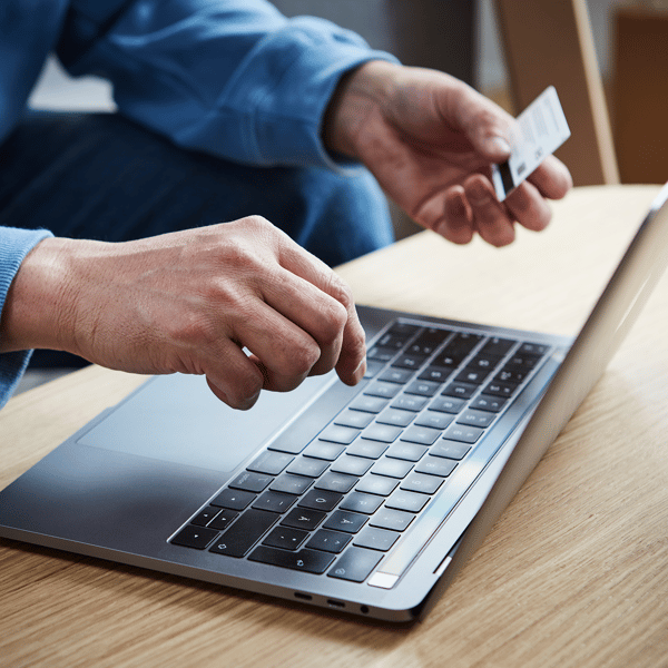 Een man heeft een creditcard in zijn hand en tikt zijn betaalgegevens in op een laptop.