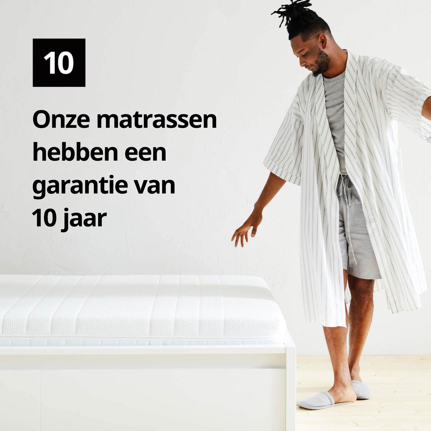 Een man in een badjas staat naast een matras en een grafisch symbool met het cijfer 10 en de tekst 'Onze matrassen hebben een beperkte garantie van 10 jaar' op de afbeelding.