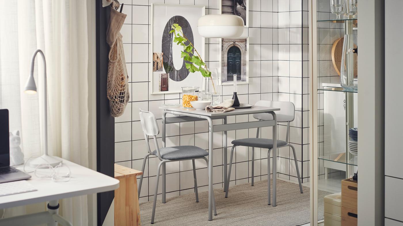 Een minimalistische studio in industriële stijl met een eetruimte die bestaat uit een grijze GRÅSALA tafel en twee stoelen naast een betegelde wand.