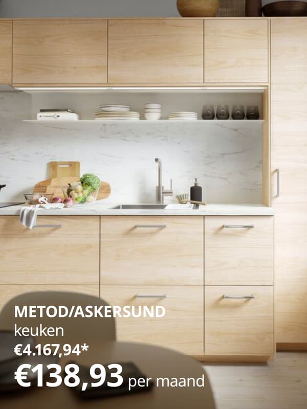 Een moderne keuken met licht houten kasten, een marmeren werkblad en backsplash, een aanrecht met groenten en keukenspullen, en open planken met servies, verlicht door natuurlijk licht van een raam.