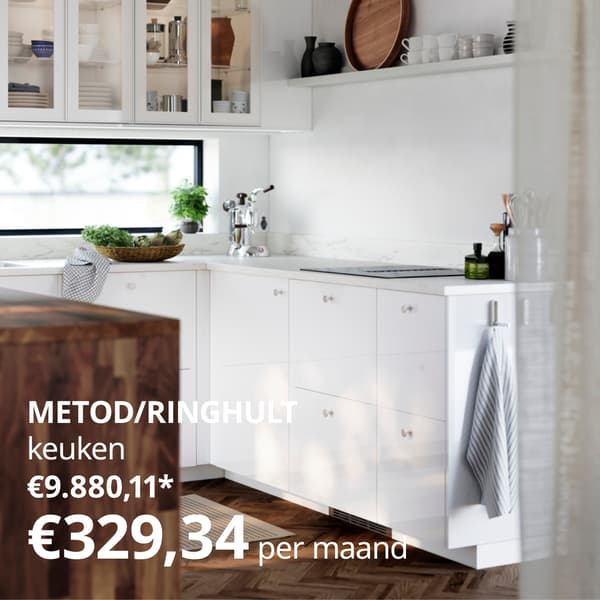 Een moderne keuken met witte kasten, een houten kookeiland, glazen bovenkasten met servies, een espressoapparaat, planten en een raam dat natuurlijk licht binnenlaat.