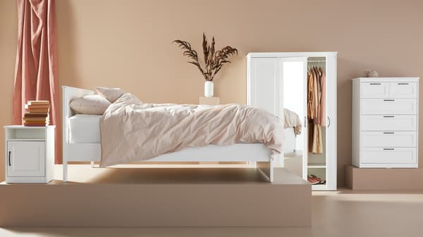 een moderne slaapkamer met een wit bed, nachtkastje, kledingkast en ladekast tegen een beige achtergrond