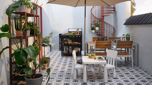 Een ommuurd terras met daarop een GRILLSKÄR buitenkeuken, SJÄLLAND tafel en stoelen en MAMMUT kindermeubels.