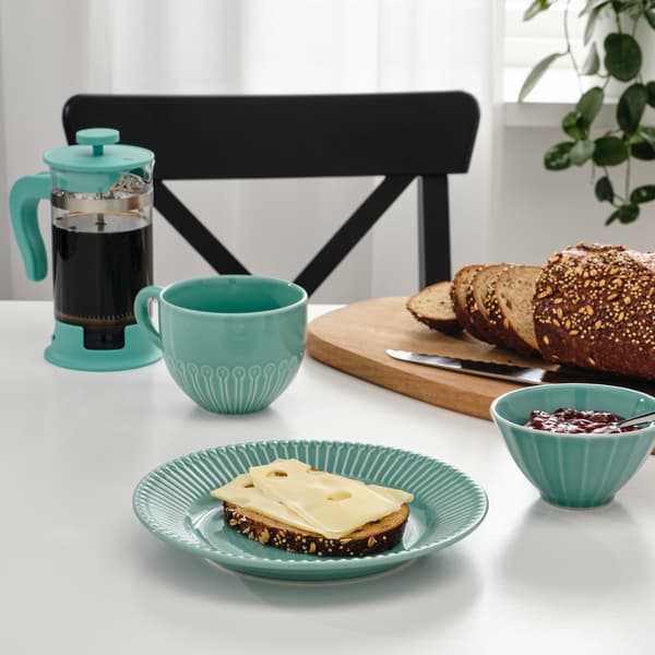 Een ontbijttafel met een STRIMMIG ontbijtbordje, kommetje en beker. Ook koffie en een broodplank staan op tafel.