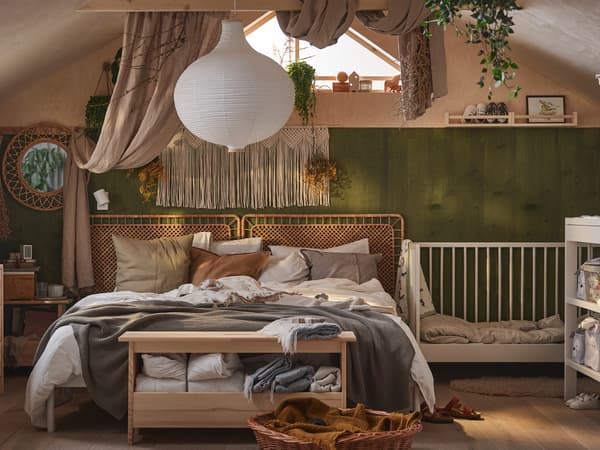 Een PERJOHAN bankje met opbergers staat aan het uiteinde van een VEVELSTAD bed met twee hoofdsteunen onder een RISBYN hanglamp.