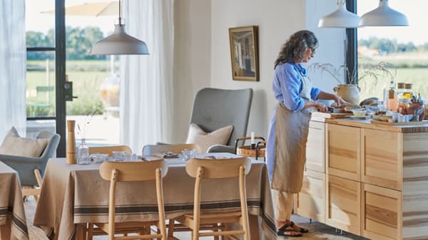 Een persoon maakt ontbijt klaar in een grote, lichte woon-en-eetkamer in traditionele stijl en met een plafond met houten balken.