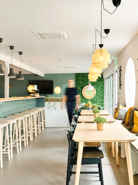 Een rij houten tafels met zwarte stoelen en daarboven rieten hanglampen