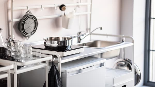 Een roestvrijstalen pan op een draagbare TILLREDA inductiekookplaat op een witte SUNNERSTA minikeuken.