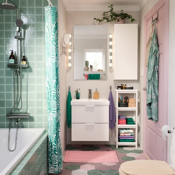 Een roze en turquoise badkamer met wastafel en wandkast in wit, een roze badmat en een douchegordijn in turquoise.