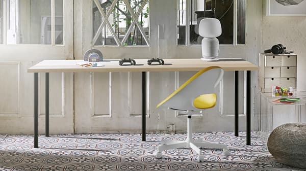 Een ruimte met zacht zonlicht waarin een lang bureau met vijf poten staat in combinatie met een LAGKAPTEN tafelblad in eikenpatroon en zwarte ADILS poten.