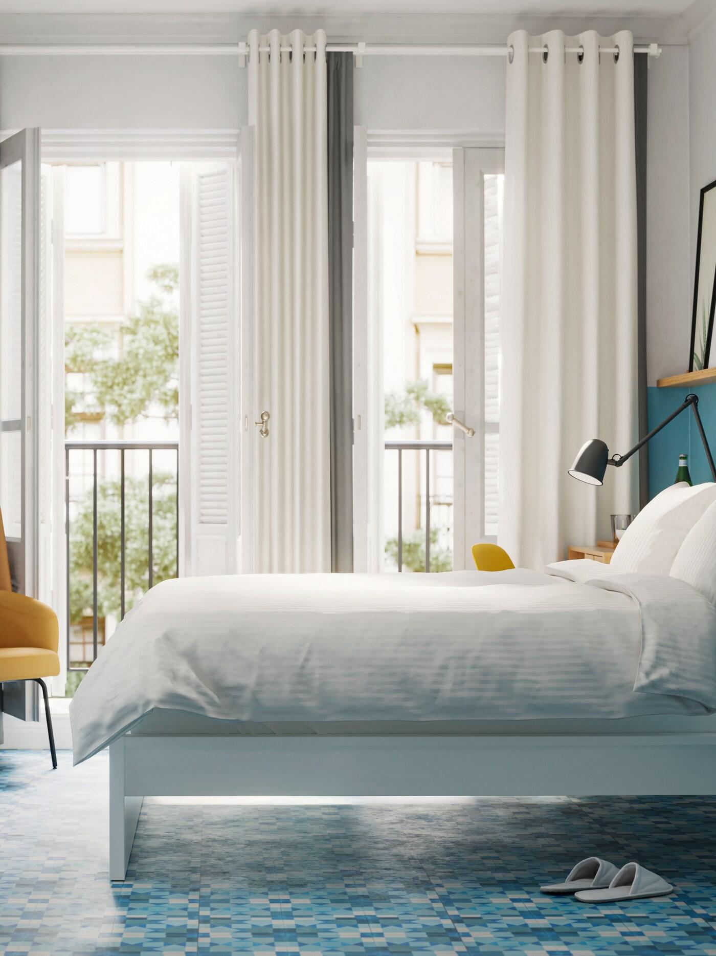 Een slaapkamer met een wit bed met wit beddengoed, blauwe muren en vloeren en openslaande deuren naar een balkon.