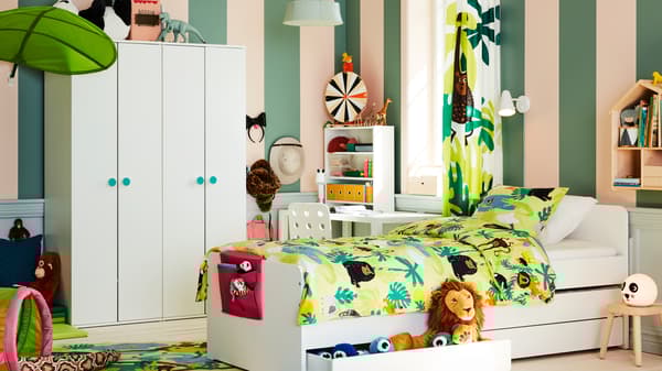 Een SLÄKT bed met onderbed en opberger in het midden van een kinderkamer met junglethema, naast twee GODISHUS kasten.