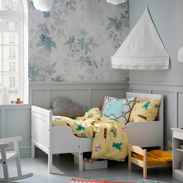 Een SUNDVIK meegroeibed in wit met geel beddengoed. Een wandgemonteerde bedhemel hangt erboven voor een knusse sfeer.
