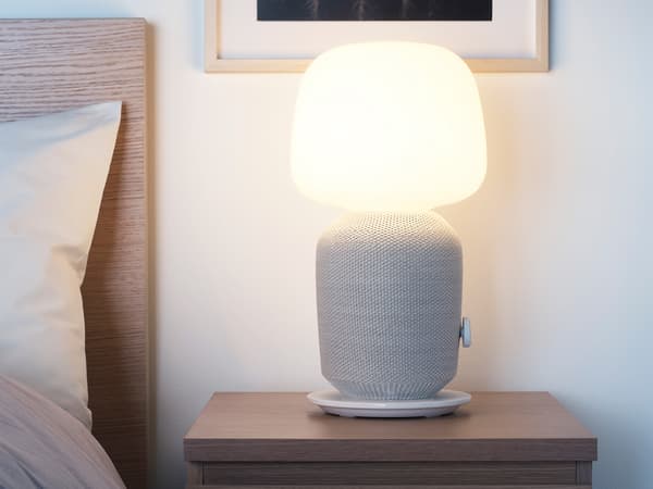 Een SYMFONISK tafellamp met wifi-speaker in wit/grijs op een nachtkastje.