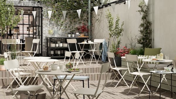 Een terras met beige opklapbare stoelen en tafels, witte vlaggetjes, tegelvloeren en een serveertafel.