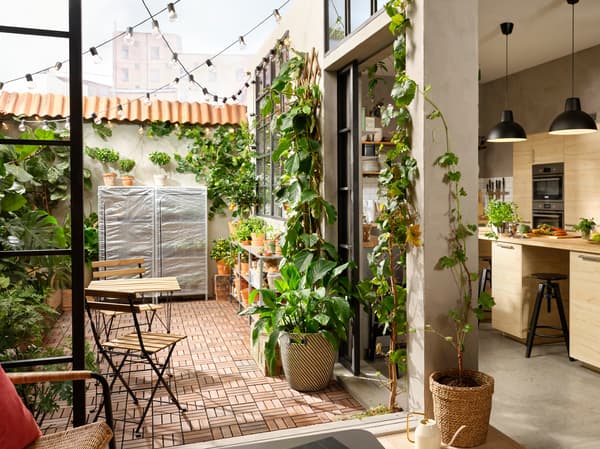 Een terras met houten vlonders, veel groene planten, hangende led-lichtsnoeren en een buitentafel met twee stoelen.