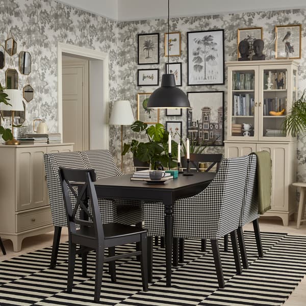 Een traditionele eetkamer met een zwarte tafel, lichte beige kastjes, zwart/witte stoelen met armleuningen en een gestreept kleed.
