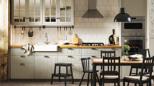 Een traditionele keuken met beige kasten, witte tegels, houten vloeren, bloemenbehang en een donkere eethoek.