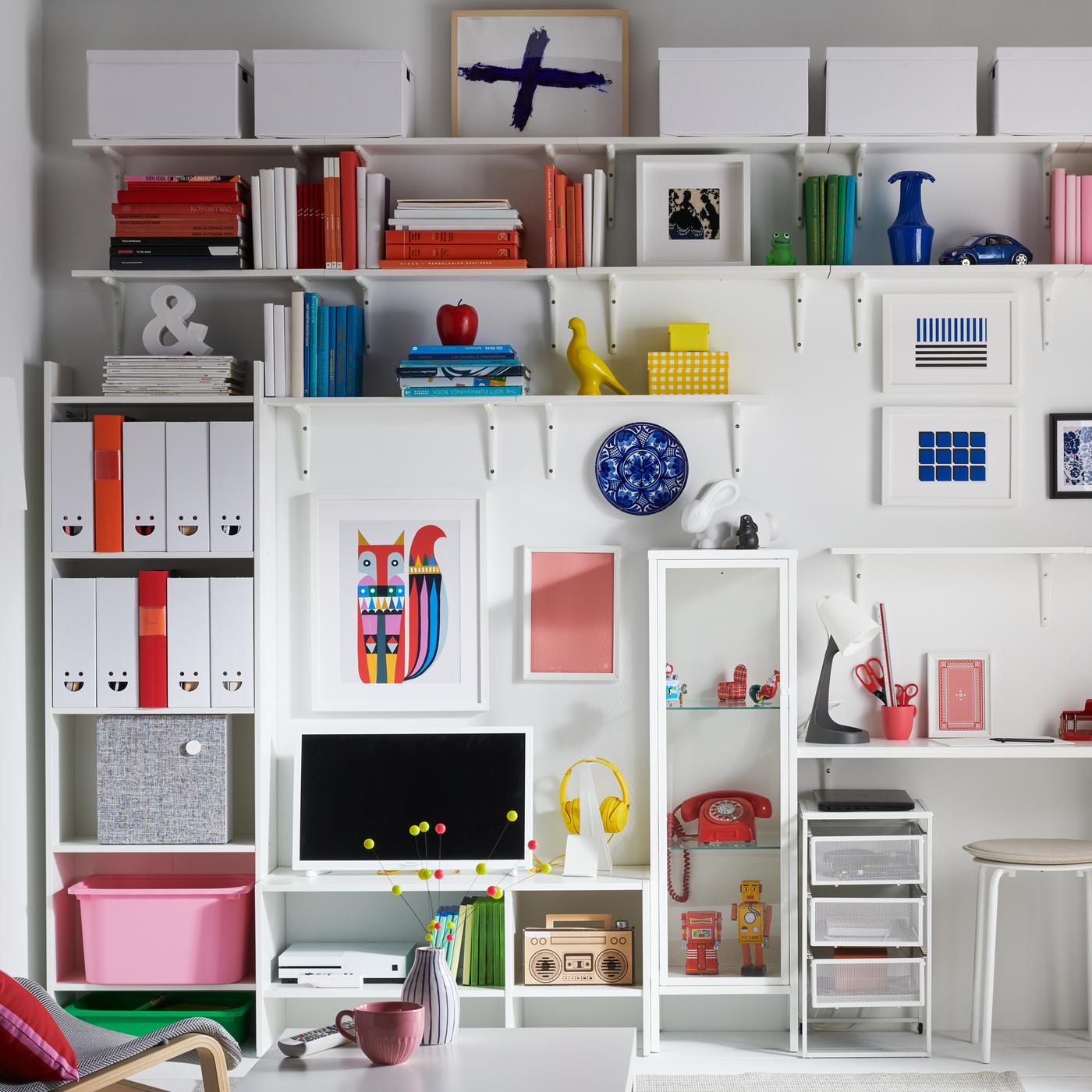 Een tv staat op een wit BAGGEBO tv-meubel voor een witte wand en omgeven door andere BAGGEBO serie opbergmeubels.