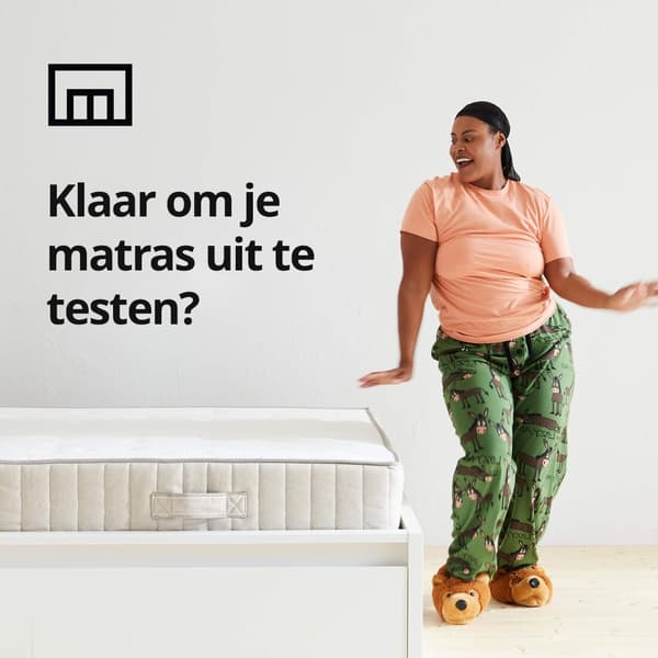 Een vrouw die in haar pyjama danst naast een bed en een winkeldoossymbool en de tekst 'Klaar om je matras uit te testen?' op de afbeelding.