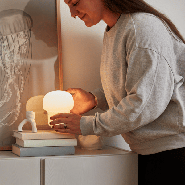 Een vrouw heeft een IKEA lamp in haar handen en wil die op een IVAR kast met decoratieve boekenstapel plaatsen.