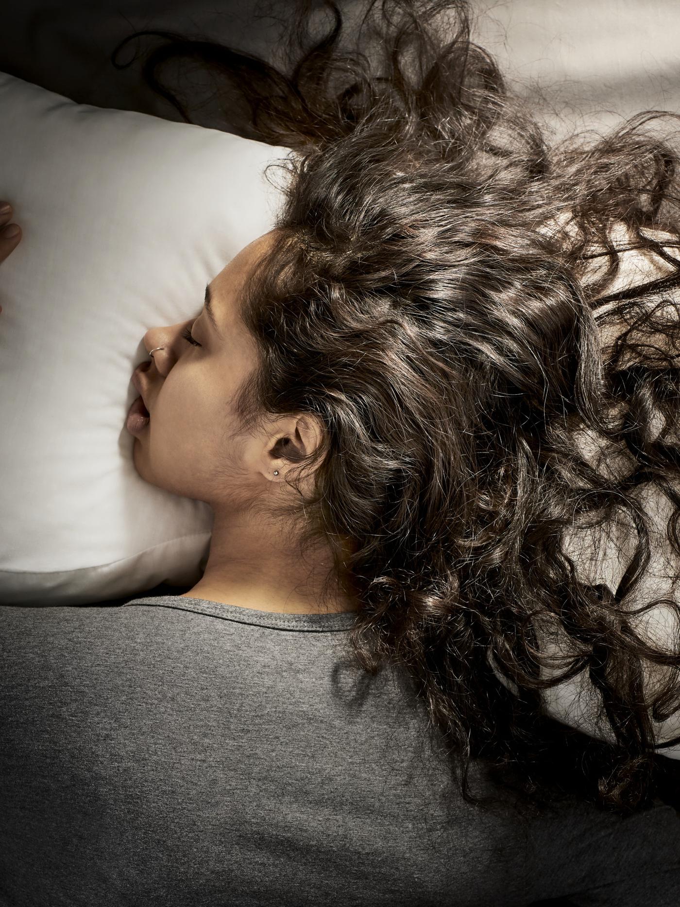 Een vrouw met bruin krullend gezicht naar beneden op een kussen liggend comfortabel slapend.