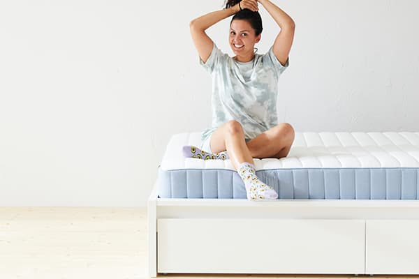 Een vrouw zit op haar bed met een glimach op haar gezicht en maakt haar haren vast in een hoge staart