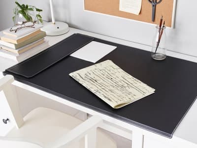 Een wit bureau met een zwarte bureau-onderlegger. Op de onderligger liggen papieren.