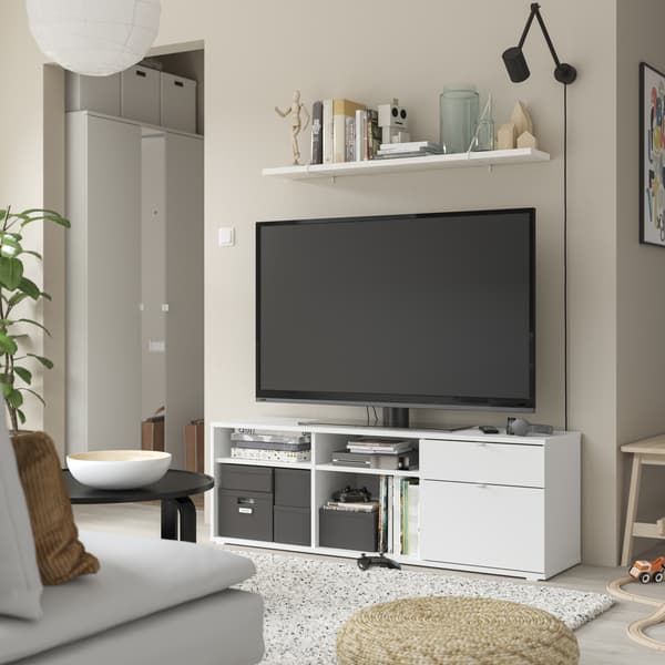 Een wit TV meubel met daarop een TV en daarboven een wandplank