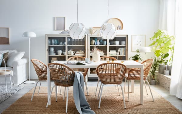 Een witte eettafel met zes rotan stoelen eromheen.