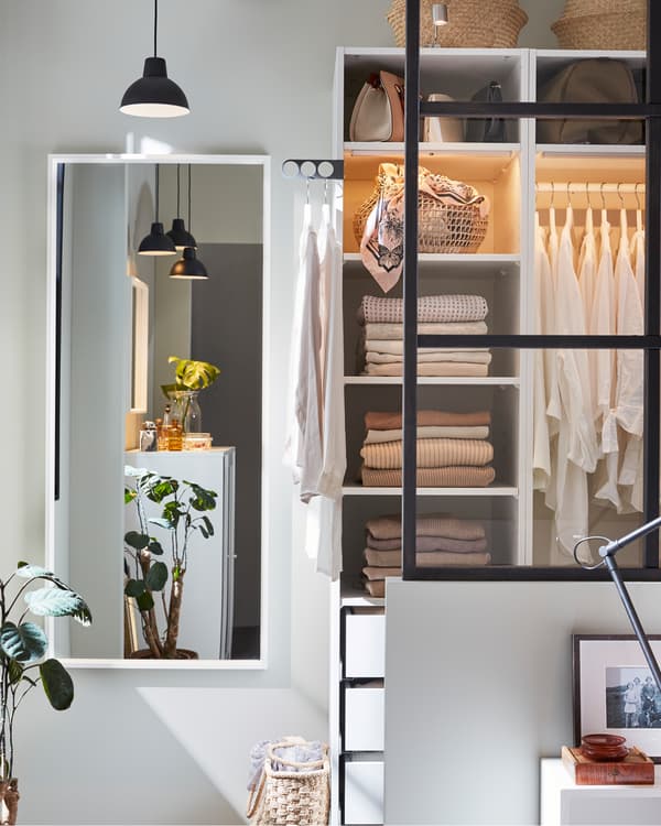 Een witte kledingkast, een zwarte hanglamp, witte spiegel en planten.