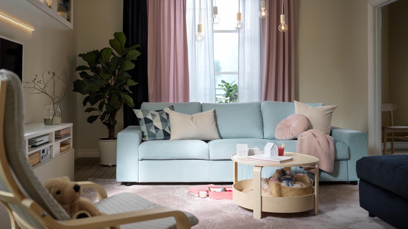 Een woonkamer in pastelkleuren met een lichtblauwe VIMLE bank, lichtroze KALKFLY gordijnen en een BORGEBY salontafel.
