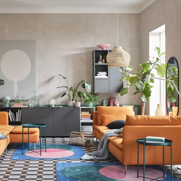 Een woonkamer met de SÖDERHAMN bank en chaise longues in oranje, een grijze kast, kleurrijke tapijten en groene dienbladtafels.