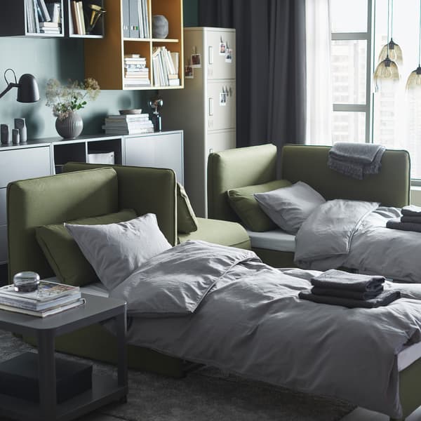 Een woonkamer met twee groene VALLENTUNA slaapbanken die als bed zijn opgemaakt.