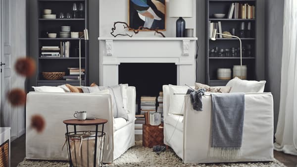 Een woonkamer met twee tegenover elkaar geplaatste witte BACKSÄLEN fauteuils tegen een achtergrond van grijze HAUGA hoge kasten die een open haard omlijsten.