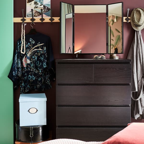 Een zwart-bruine ladekast, een zwarte wandlamp, zwarte spiegel, dennenhouten rekken met grijze haken en een blauwe opbergdoos met deksel