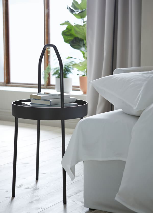 Een zwart, rond IKEA BURVIK tafeltje met een dunne lichte handgreep in een woonkamer.