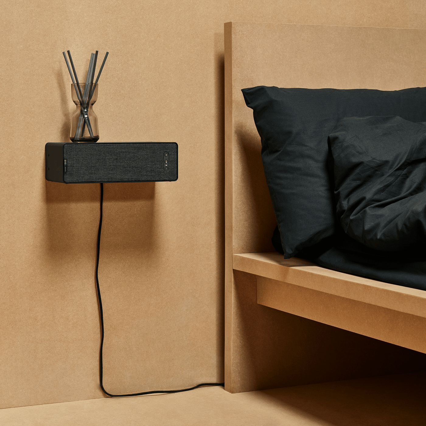 Een zwarte boekenkastspeaker bevestigd aan de muur naast het bed