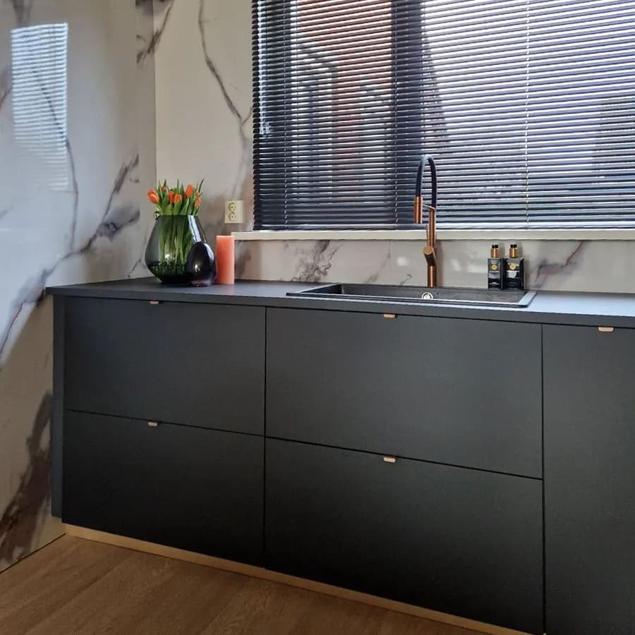 Een zwarte keuken met kleine handgreepjes en een zwarte kraan