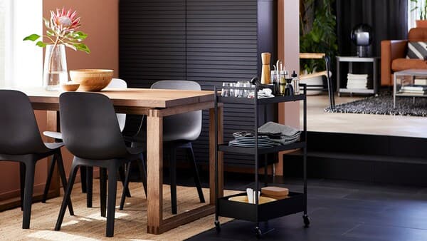Eetkamer met antraciet stoelen, een tafel van gebeitst eikenfineer, zwart opbergsysteem, een juten vloerkleed en een roltafel met servies.