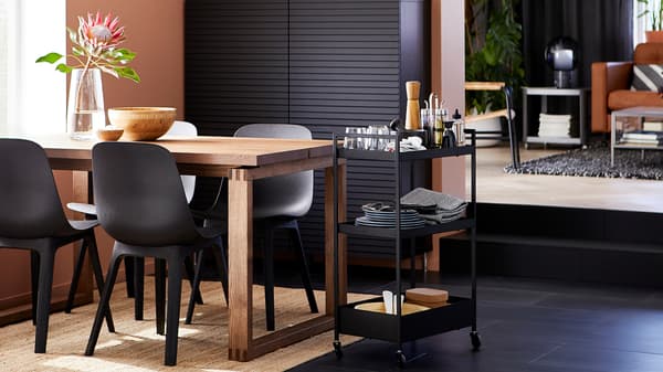 Eetkamer met antraciet stoelen, een tafel van gebeitst eikenfineer, zwart opbergsysteem, een juten vloerkleed en een roltafel met servies.