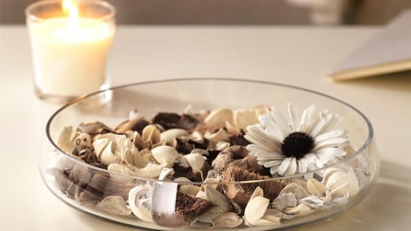 Egy alacsony üvegtál potpourrival, mellette egy pohárban égő gyertya.