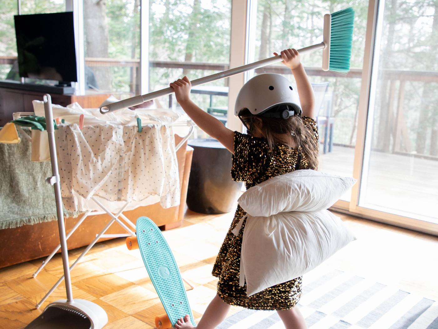 Egy bukósisakot viselő kislányt látunk egy gördeszkával, amint a feje felett tartott PEP-PRIG partvissal áll egy nappaliban, egy száradó ruhákkal megpakolt JÄLL szárítóval szemben.