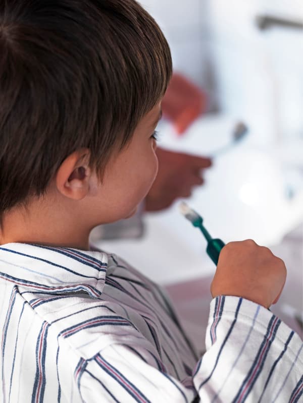 Egy csíkos pizsamás fiú a fogát mossa.