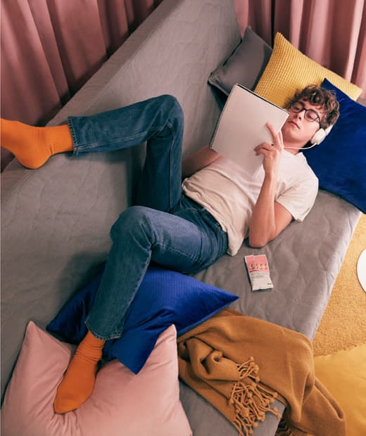 Egy diák pihen a szürke kanapén, zenét hallgat és tanul.