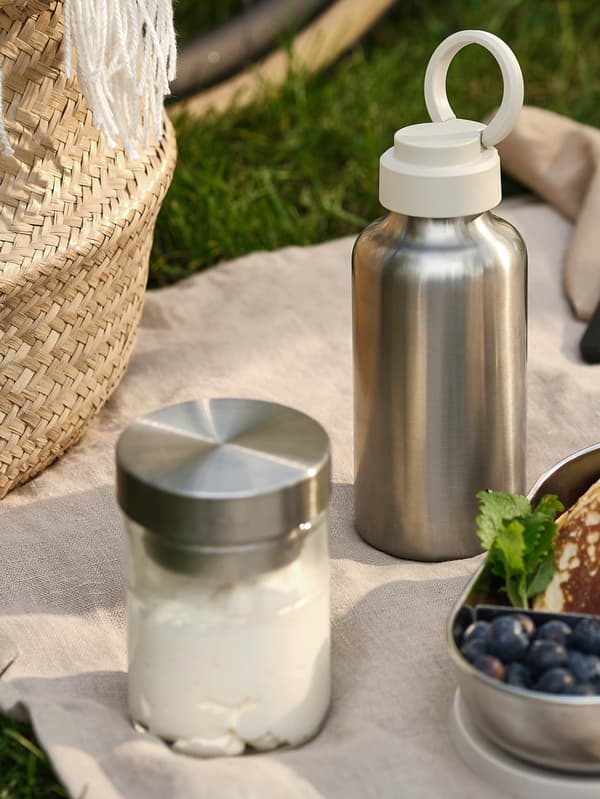 Egy fém ENKELSPÅRIG kulacs és egy DAGKLAR üvegedény fémbetéttel látható egy bézs takarón.