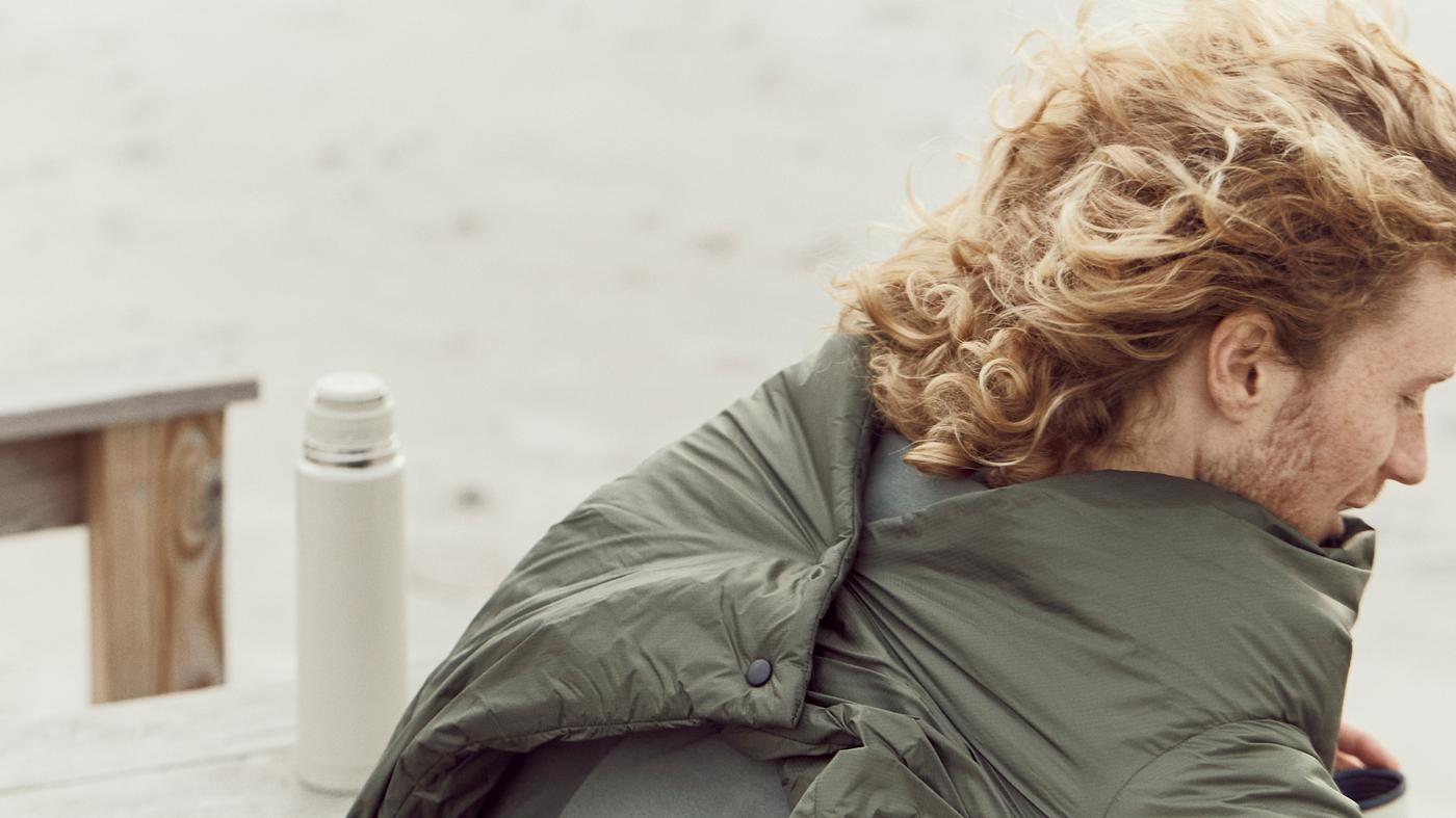 Egy férfi a parton FÄLTMAL paplanba van tekerve, ami a hátán praktikus gombokkal rögzítve van.