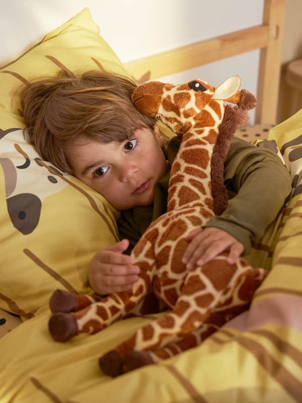 Egy fiú az ágyban egy kis SANDLÖPARE zsiráfot ölel magához.