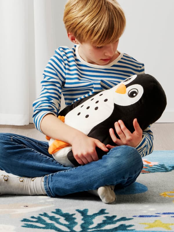 Egy fiú pingvinformájú díszpárnát tart a kezében.