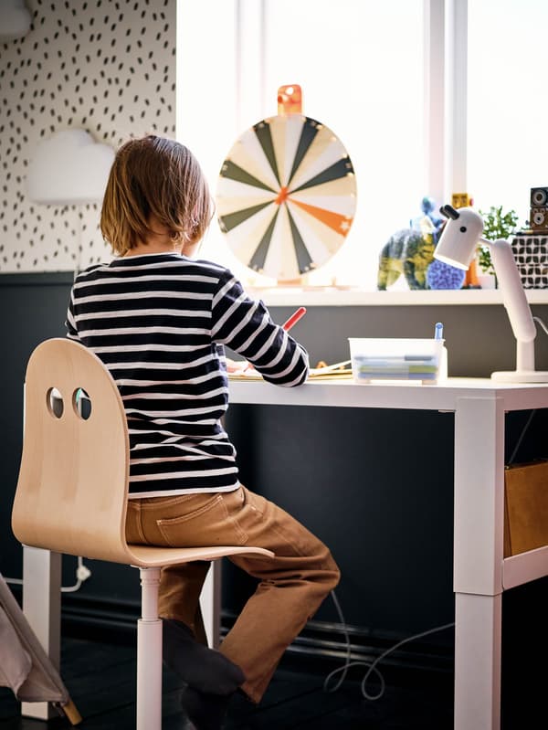 Egy fiút látunk csíkos felsőben, amint VALFRED SIBBEN széken egy fehér PÅHL íróasztal mellett ül.